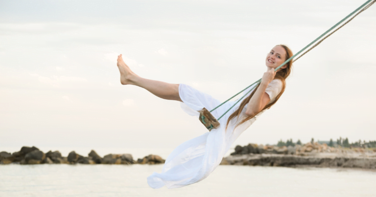 A girl in a white dress joyfully swings on a swing, embracing her inner child.