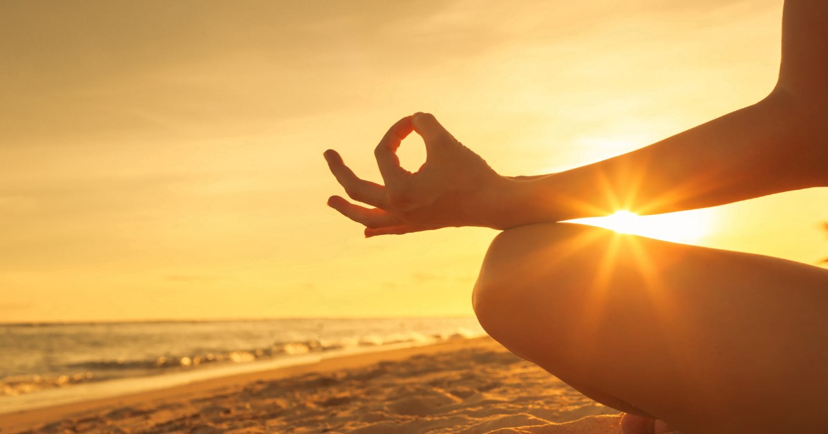 A close-up of a person's hand displaying a mudra gesture during a serene sunset on the beach, exuding inner peace amidst the vastness of the water.