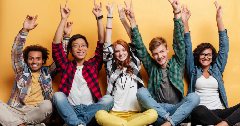 Five young adults seated in a row against a yellow background, smiling and raising their hands with peace signs. they exude a lively and joyful atmosphere, fostering healthy relationships.