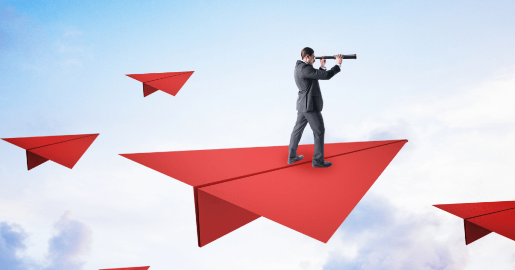 A man in a business suit stands on a large red paper plane, using a telescope to look ahead, with smaller paper planes and a cloudy sky in the background, looking for life crew.