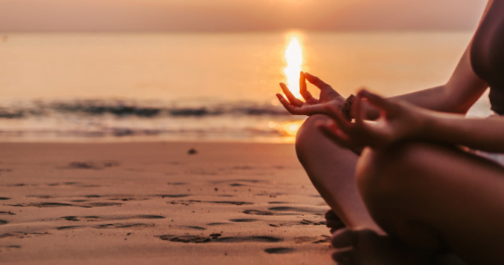 Woman finding inner peace while meditating on beach at sunset.