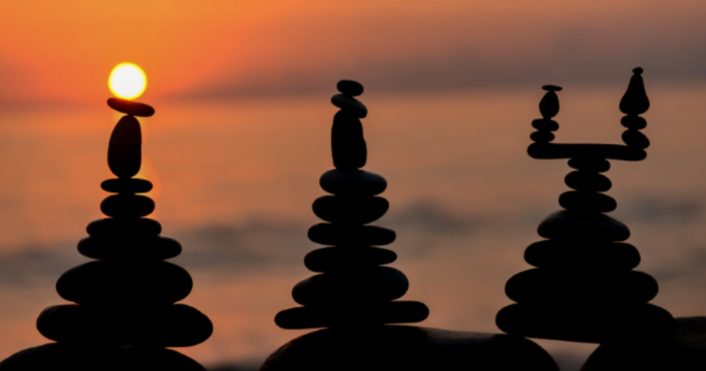 Balanced stones on a beach at sunset, a metaphor for achieving a balanced life through different types of rest.