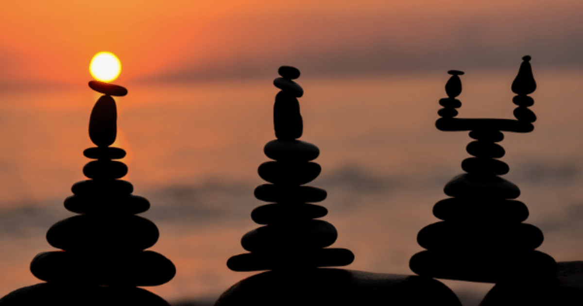 Balanced stones on a beach at sunset, a metaphor for achieving a balanced life through different types of rest.