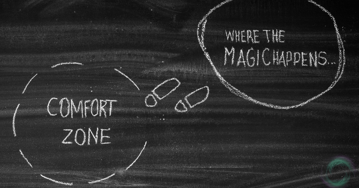 A blackboard divided into two sections. The text "comfort zone" is written in large letters on the left side. The right side displays the phrase "where the magic happens" written in cursive.